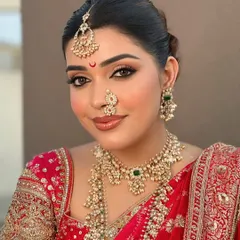 A close-up of a beautiful bride wearing a layered Kundan necklace set with a delicate nath and maang tikka. The combination of pearls and a central emerald drop adds a touch of color and sophistication.