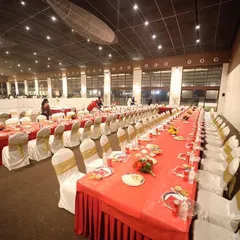 A wide shot of the setup for a 'Shukraana' party at Anantia Palace Ground. The long tables are perfectly arranged with red tablecloths and elegant chair covers, ready for the guests to arrive.