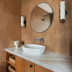 In the East Coast Residence, this bathroom showcases our focus on integrating storage without compromising on style. The wooden vanity with open shelving provides functionality, while the warm-toned tiles and unique sconces add character.