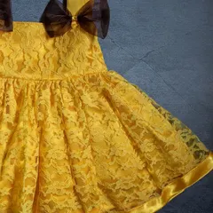 A close-up of a vibrant yellow lace dress. The delicate lace overlay and the contrasting brown bows on the shoulders make this a perfect summer party dress.