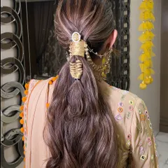 A textured ponytail with a unique, woven hair accessory. This style combines the ease of a ponytail with the elegance of detailed craftsmanship, perfect for a festive look.