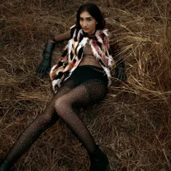 An overhead shot from a fashion story set in a dry, grassy field. The model's pose and the textures of the faux fur and sparkling tights contrast with the rustic, natural setting.