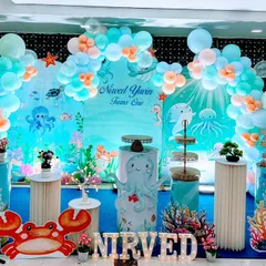 An immersive under the sea aqua theme for a first birthday celebration. This vibrant setup features a custom ocean backdrop, themed cake stands, character cutouts of a crab and turtle, and a balloon garland in seafoam green and pastel blue.