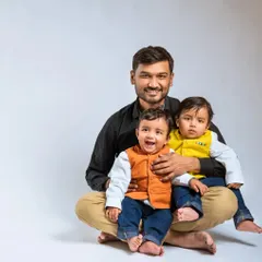 A proud father with his twin baby boys. The boys' colorful vests add a playful touch to this studio portrait, highlighting the joy and energy of life with twins.