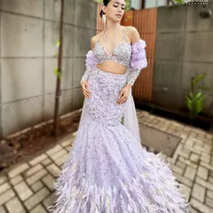 A breathtaking western-inspired bridal look in a lilac gown with feather details. The makeup is kept sleek and modern, with a wet-look hairstyle and soft purple tones on the eyes.