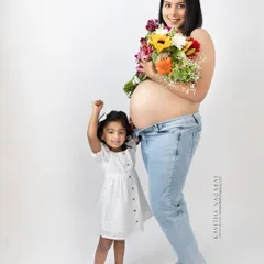 A future big sister gives a cheer while standing next to her mother's baby bump. A joyful and candid moment capturing the excitement of a growing family.