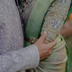 A detail shot focusing on the couple's hands and their exquisite traditional attire. This artistic close-up highlights the intricate embroidery and the gentle touch that speaks volumes.