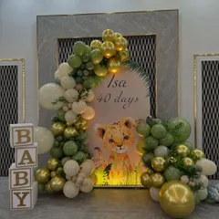 A cute baby lion theme for a '40 days' celebration. This setup includes a personalized backdrop, a balloon garland in green and gold, and 'BABY' display boxes.