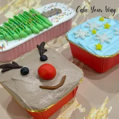 My mini loaf cakes get a festive makeover for Christmas. Here you can see them decorated as a reindeer, a Christmas tree, and a snowy sky, making them a cute and delicious holiday treat.