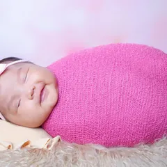 A beautiful smiling baby girl, happily swaddled in a bright pink wrap. It's a joy to capture these happy expressions when babies are awake and content.