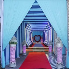 A unique tunnel-style entrance with blue and white drapes. The heart-shaped floral arrangement at the end of the tunnel adds a romantic touch for a wedding or reception.