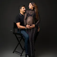 A truly show-stopping look. This expecting mother is the definition of glam in a sheer, embellished gown that beautifully showcases her baby bump against a classic dark studio background.