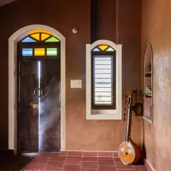 The beauty of simplicity, or *Saralatheya sobagu*, is captured in this corner of the Doddaballapura mud house. The walls are finished with a simple mud plaster, the door is reclaimed wood, and the light filtering through stained glass brings a quiet warmth, proving that a home doesn't need to be loud to be beautiful.