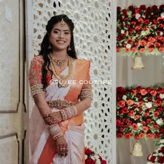 The pure joy of a bride on her wedding day. She is wearing a custom orange and white Kanchipuram saree, complemented by a hand-embroidered blouse with detailed work on the sleeves, designed to make her feel special.