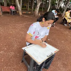A student fully absorbed in her work during an outdoor sketching session. We provide portable stools and boards so our artists can comfortably focus on capturing the scene in front of them.