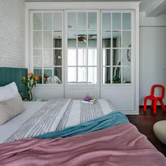 A wider view of the 'Urban Oasis' bedroom, showing the interplay of textures. The white brick wall, the mirrored wardrobe, and the colorful textiles on the bed create a vibrant yet harmonious space.