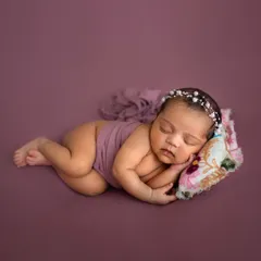 A full-body shot showing the classic newborn pose. The tiny floral pillow adds a sweet detail to this simple and serene portrait.