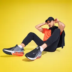 This image from a shoe campaign uses a bright yellow background to create a high-contrast, energetic look. The relaxed pose allows for a clear view of the sneakers from the side, showcasing their design and color accents.