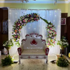 An intimate and magical baby shower setup at home. A delicate floral arch against a backdrop of white curtains and fairy lights creates a cozy and elegant space for the mom-to-be.