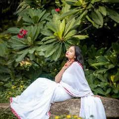 Serenity in nature. This portrait, taken in a lush green setting, uses soft, natural light to create a peaceful and elegant mood, highlighting the simple beauty of the white saree.