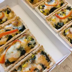 Bite-sized mini quiches with a corn and spinach filling, baked in rectangular tart shells and packed neatly in a box, ideal for parties and high-tea events.