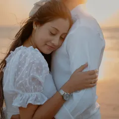 A soft and tender moment during a sunset beach shoot. The bride rests her head on the groom's chest, and the warm, golden light creates a beautifully romantic and peaceful atmosphere.