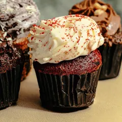 A close-up of a red velvet cupcake, showing the detail of the cream cheese frosting and red sprinkles. We capture every delicious detail to make the food look its best.