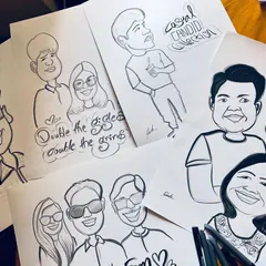 A flat lay of several finished caricatures, showing the variety of my work, from individuals to couples and groups.