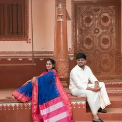 A relaxed portrait in front of a traditional house. The bride's vibrant blue and pink saree looks stunning against the earthy tones of the background, creating a beautiful, rustic feel.