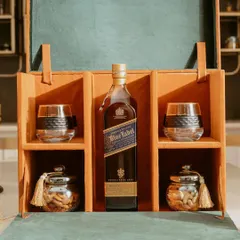 A full view of our sophisticated whiskey hamper. The elegant leatherette box opens to reveal a curated selection of a premium whiskey bottle, two glasses, and jars of almonds and cashews.