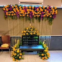 This Haldi setup combines traditional and modern elements. A curtain of delicate white tuberose (rajnigandha) strings is topped with a colorful arrangement of yellow gerberas and purple statice, creating a unique and fragrant backdrop.