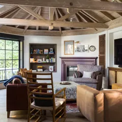 In this Saratoga family room, a repositioned stone fireplace becomes the anchor. The space is filled with deep-seated sofas and a rocking chair, perfect for cozy evenings. The exposed wood beams on the ceiling add rustic warmth, creating an intimate and inviting atmosphere.