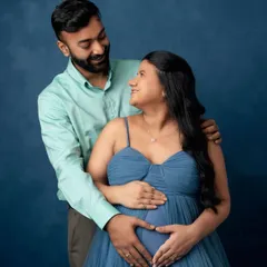 The look of love and anticipation. This intimate couple's maternity portrait against a deep blue backdrop highlights the connection and shared excitement of expecting parents.