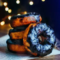 A stack of chocolate-glazed donuts set against a dark background with soft, warm lights. This moody photography style highlights the rich texture of the glaze and creates a cozy, late-night treat vibe.