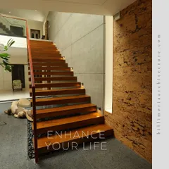 The floating wooden staircase in the "Waterfront Home" is a sculptural element in itself. It rises alongside a textured cork wall and overlooks the indoor water feature, blending natural materials and modern design.