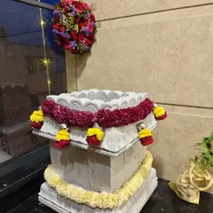 Simple and elegant floral decor for a housewarming, with garlands of red and yellow flowers adorning a traditional stone Tulasi Katte.