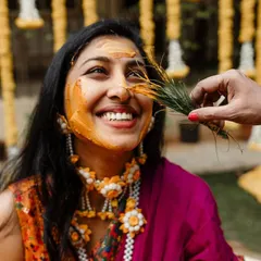 A playful moment during a Haldi ceremony, with a guest gently applying turmeric to the bride's face. These are the candid, happy memories we love to preserve.