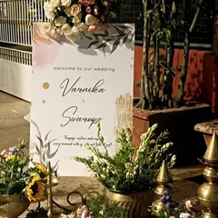 A personalized welcome sign for Varnika and Swarrop, elegantly displayed with traditional brass decor and floral arrangements.