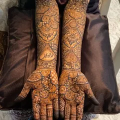This bridal design incorporates the bride's name in elegant Arabic script on the forearm. The surrounding patterns are a mix of floral bursts and intricate line work for a balanced and personal look.