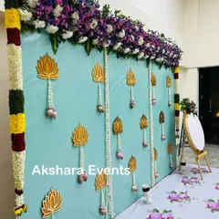 A modern backdrop design featuring a mint-colored fabric wall, hanging lotus motifs, and a rich border of purple and white flowers.