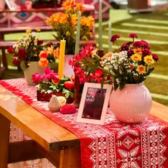 A rustic yet vibrant tablescape featuring a traditional patterned runner, colorful floral arrangements in a pink vase, and tall candles, perfect for a lively daytime event.