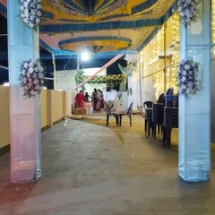 A glimpse of an outdoor wedding reception being set up under a large tent. The pillars are wrapped in light blue and white fabric with floral accents, and the ceiling is draped in blue and yellow cloth.