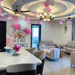 Welcome your little one home to a room filled with love. This is a beautiful living room decoration with "Welcome Home" foil balloons, pink and white balloon clusters on the ceiling, and transparent 'BABY' boxes for a modern touch.