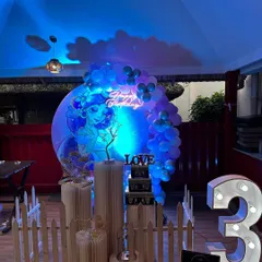 A mermaid-themed party with dramatic blue lighting. The setup includes a circular backdrop with a mermaid graphic, a neon sign, and a large marquee number '3'.