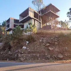 A view of the hillside home from the road below, highlighting its commanding presence and integration with the natural contours of the land. The scaffolding hints at the multi-level design taking shape.