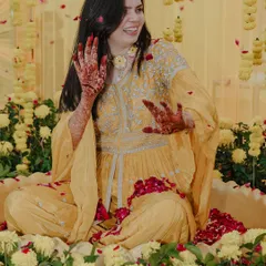 The bride enjoying a shower of rose petals during her Haldi ceremony, her face lit up with a joyful smile.