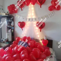 A classic romantic birthday surprise with a bed full of red heart-shaped balloons and a fairy light canopy.