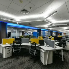An open-plan office layout with modern workstations and low partitions to encourage communication. An orange phone booth provides a quiet, soundproof space for private calls.
