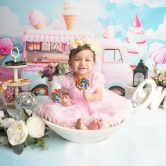 The birthday girl sits in a bowl holding lollipops, surrounded by the sweet Candyland theme. Her happy expression is the centerpiece of this fun milestone photo.
