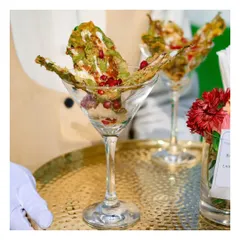 A creative vegetarian appetizer of Palak Patta Chaat served elegantly in a martini glass, combining crispy spinach leaves with tangy chutneys and pomegranate seeds.